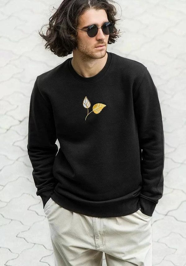 a man with long curly hair wearing a black sweatshirt with a yellow leaf on it